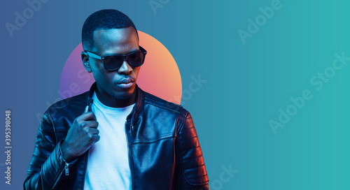 Banner of stylish black young man wearing leather jacket and sunglasses, isolated on blue gradient background