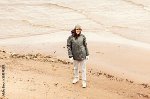 Portrait of beautiful young environmental volunteer smiling at camera standing on sea coast during beach cleaning