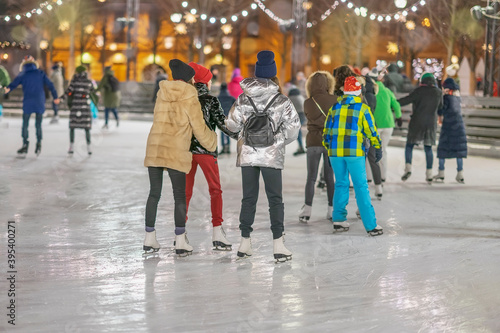 Happy Girlfriends ice skating on rink in city park. Healthy outdoor winter activity