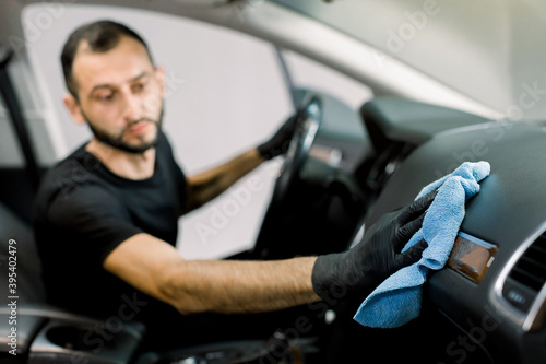 Cleaning service, car detailing concept. Young man, auto service worker, washing a car interior, console and dashboard with microfiber cloth, in a professional car wash. Fpcus on a hand with cloth