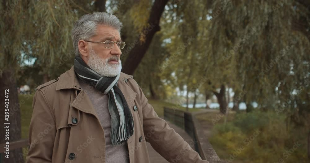 Thoughtful handsome man in brown coat standing in park, recreation at weekend Thoughtful handsome man in brown coat standing in park, recreation at weekend