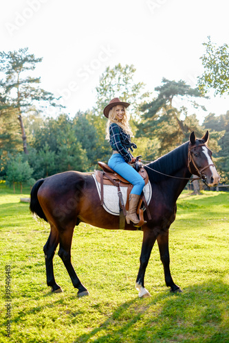 Smilng pretty young cowgirl. Sitting on her horse on the ranch. Woman in plaid shirt and cowboy hat.