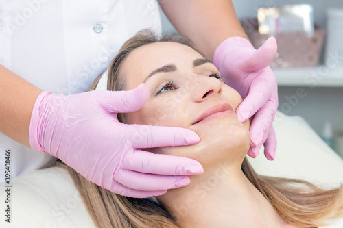 Cosmetological facial massage. beautician doing facial massage to a satisfied beautiful young woman