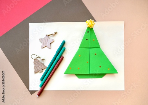 The simbol of Christmas and New year is a paper Chrismas tree on a beige background. Origami green Chrismas tree. The concept of DIY. On lene instructions step by step.  photo