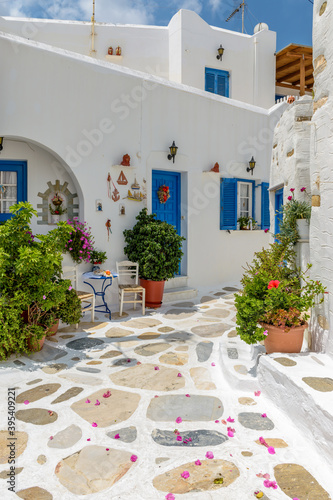Picturesque alley in Prodromos Paros greek island with whitewashed traditional houses with blue door and flowers all over.