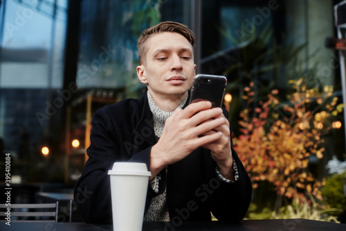 A man is sitting at a table in a cafe on the street Holding a Cup of coffee and chating