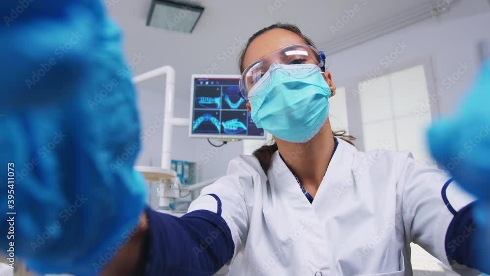 Patient point of view to dentist in protective mask holding tools examining person with toothache sitting on stomatological chair while nurse preparing tools for surgery. Patient point of view to dentist in protective mask holding tools examining person with toothache sitting on stomatological chair while nurse preparing tools for surgery.
