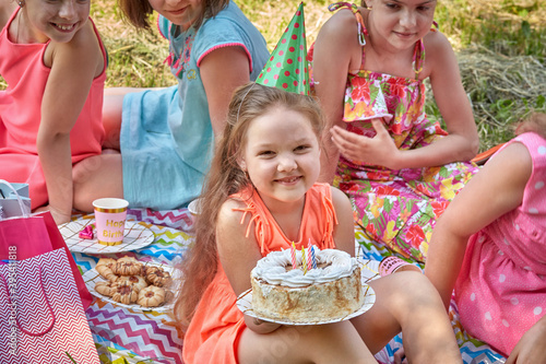 Beautiful little girl holding a birthday cake in a large group of friends. Celebrate your birthday in nature.