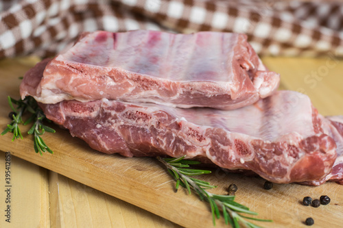 Uncooked pork ribs on a wooden board with rosemary and allspice peas on a kitchen towel background.