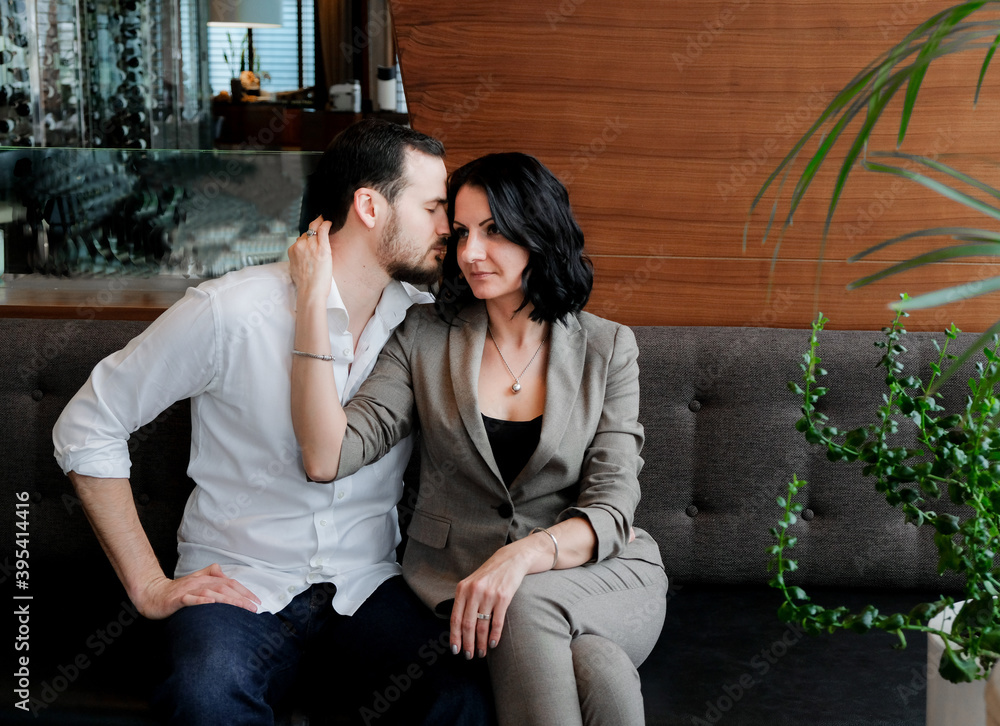 Business love. Fashionable adult couple. Man in a white shirt and woman in brown suit. They sitting on sofa. Business love. Fashionable adult couple. Man in a white shirt and woman in brown suit. They sitting on sofa.