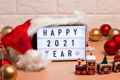 Banner with inscription Happy 2021 Year on interior lightbox with Santa's hat and Christmas balls and little toy train. Christmas Time.