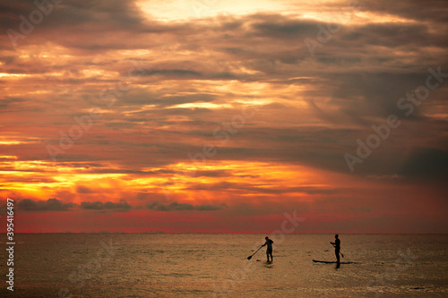 Sea sup surfing under amazing dark sunset sky. Two people on Stand Up Paddle Board. Orange sky. Paddleboarding Concept. Phuket. Thailand. © Semachkovsky 