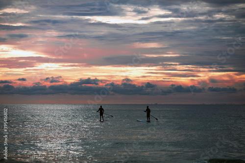 Sea sup surfing under amazing dark sunset sky. Two people on Stand Up Paddle Board. Orange sky. Paddleboarding Concept. trips to warm destinations. Phuket. Thailand.