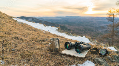 Binoculars map compass and mug on the background of nature mountains in the sunset. The concept of a halt, tourism travel, trip. Navigation, route
