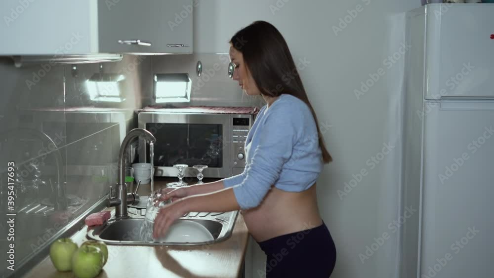 a pregnant woman of European appearance stands in the kitchen washing a glass glass. Work hard during pregnancy concept a pregnant woman of European appearance stands in the kitchen washing a glass glass. Work hard during pregnancy concept