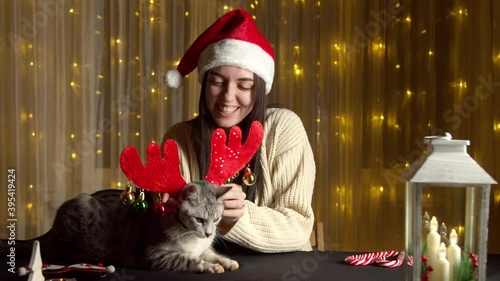 Stylish happy girl in santa hat playing with cute cat