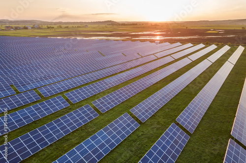 Blue solar photo voltaic panels system producing renewable clean energy on rural landscape and setting sun background.
