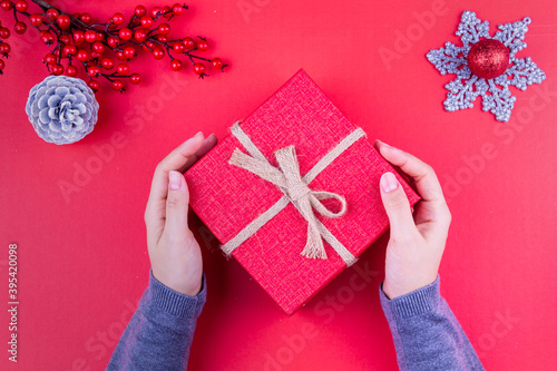 hands of girl holding gift box next to red new year concept and white cone (ID: 395420098)