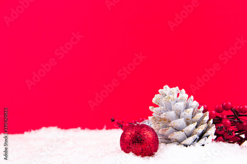 Red kokina flower, white pine cone and bright red new year ornament on red background and snowy backdrop for Christmas (ID: 395420833)