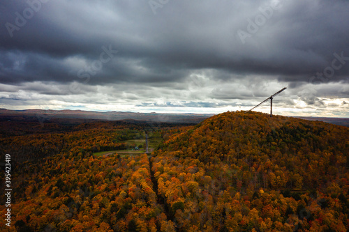 Beautiful view of Copper Peak ski jump and hill sticking up high into the cloudy and overcast sky above surrounded by colorful red, orange, yellow and green tree foliage.