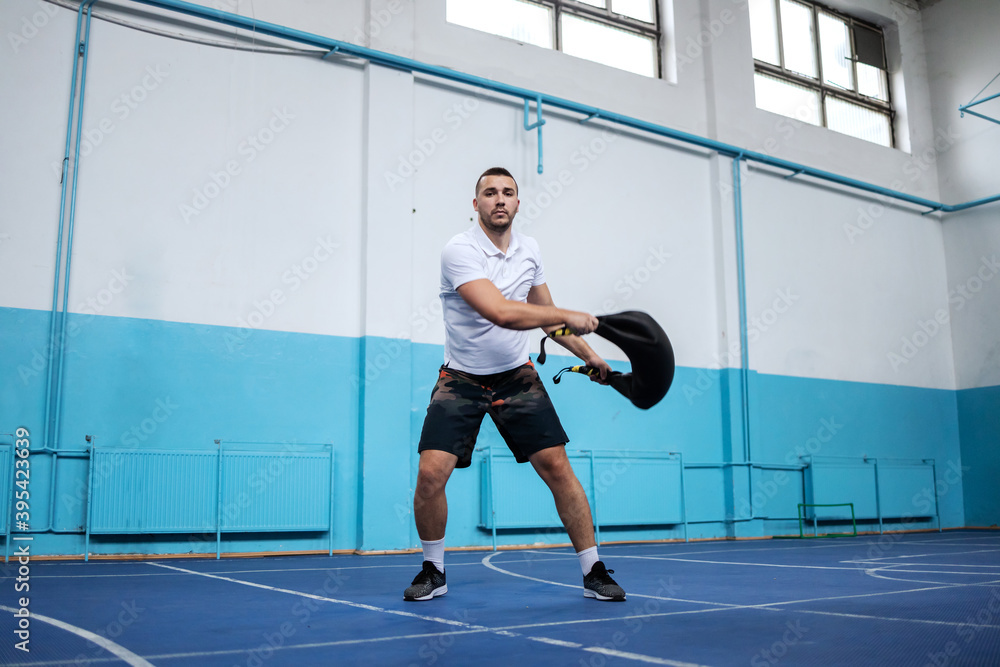Dedicated strong muscular sportsman doing exercises with bulgarian sack while standing in sport hall.