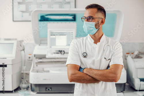 Doctor with face mask and stethoscope around his neck standing in hospital during corona virus outbreak.