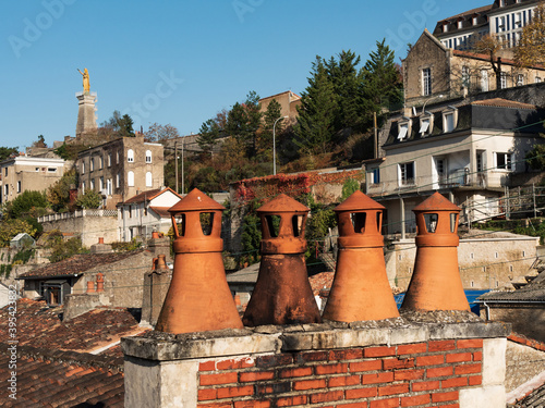 View of the city of Poitiers, France. In the foreground, there are roofs and chimneys. In the background, there is the famous statue of Notre-Dame des Dunes. photo