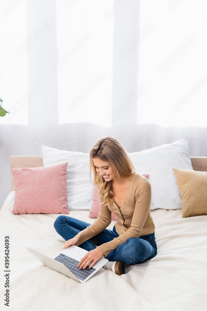woman working on laptop while sitting on bed at home woman working on laptop while sitting on bed at home