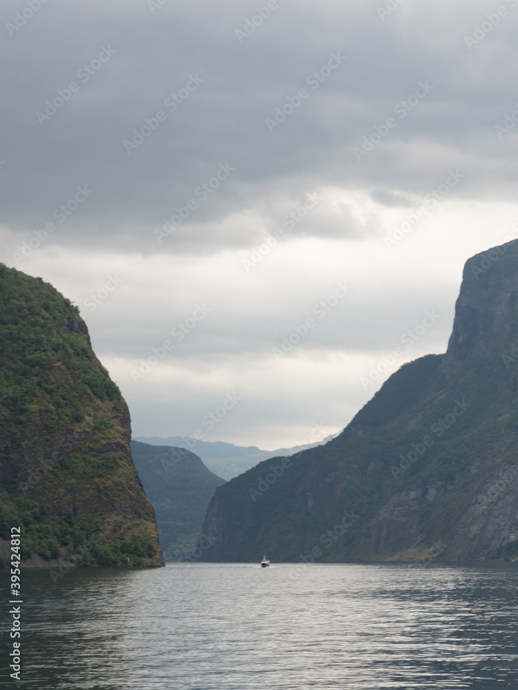 View on a Fjord in Norway, Europe, during a cruise north of the city of Bergen. Photographed vertically. Many mountains in the background. Cloudy sky.