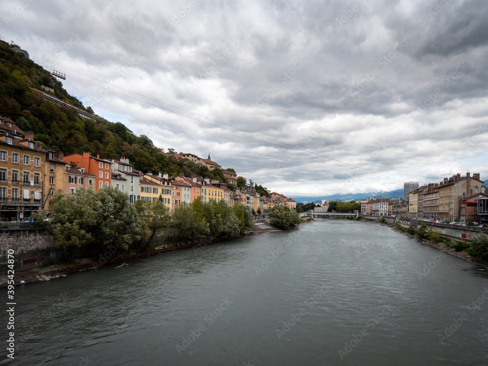 View of the Isère River and the Saint-Laurent district on the left. Photographed in Grenoble, a city in the French Alps. Cloudy sky.