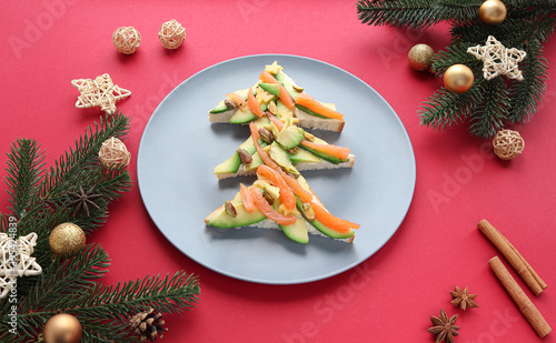 Christmas sandwiches with cheese, salmon and avocado in the form of a Christmas tree on a red background.