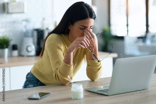 Stressed business woman working from home on laptop looking worried, tired and overwhelmed while sitting in the kitchen at home. photo