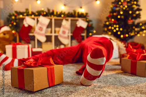 Photography Gift box tied with red ribbon beside tired drunk Santa lying asleep on floor in
