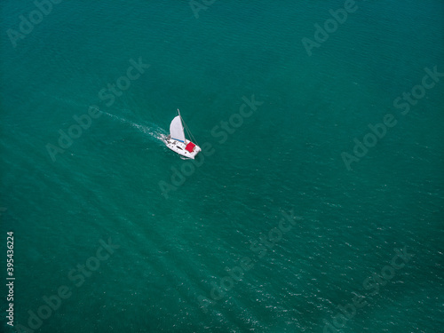 Sailing ship yachts with white sails and red awning from the sun for passengers at open sea. Aerial - drone view to sailboat in windy condition