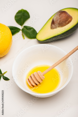 Bowl with honey and dipper, fresh avocado, lemon and rose leaves on white, stock image