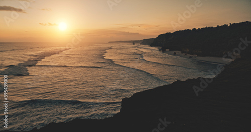 Relax serene seascape sunset silhouette of ocean cliff coast aerial view. Cinematic sun set light at dark rock wall. Amazing sea bay waves water washed sand beach of Bawana, Sumba Island, Indonesia