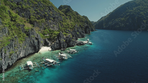 Closeup aerial view of boats at ocean cliff coast with green tropical forest. Beautiful exotic nature landscape at mountain island of Palawan, Philippines, Asia. Cinematic drone soft light shot