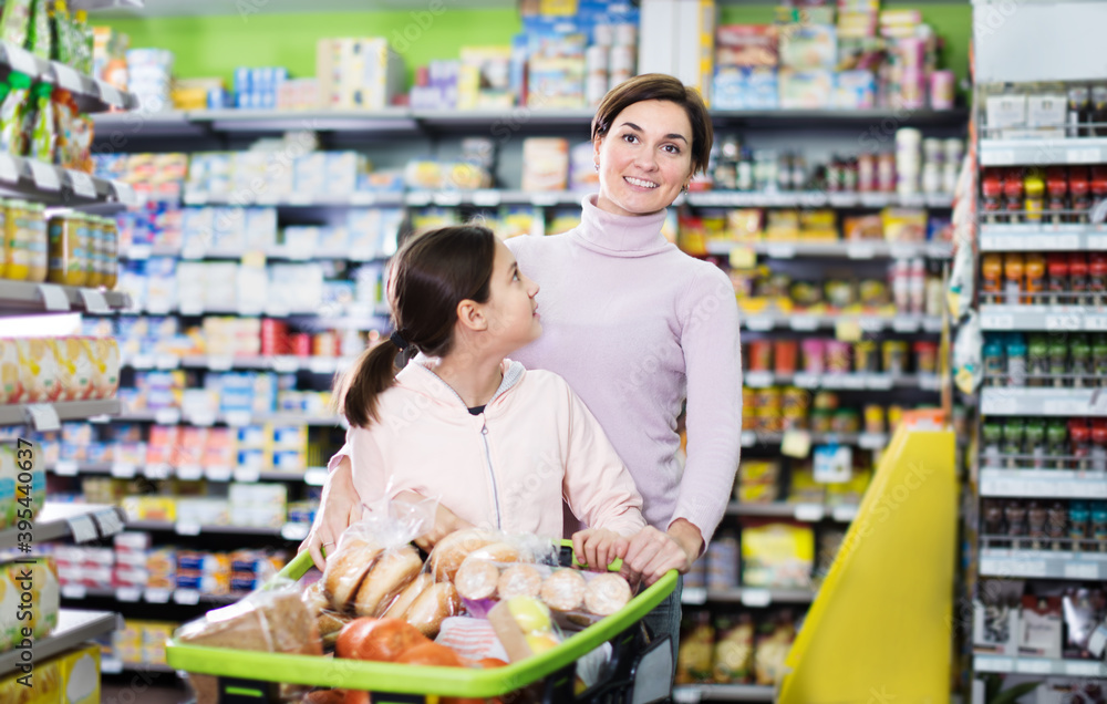 Young woman customer with girl looking for a food supplies at the supermarket. Focus on woman