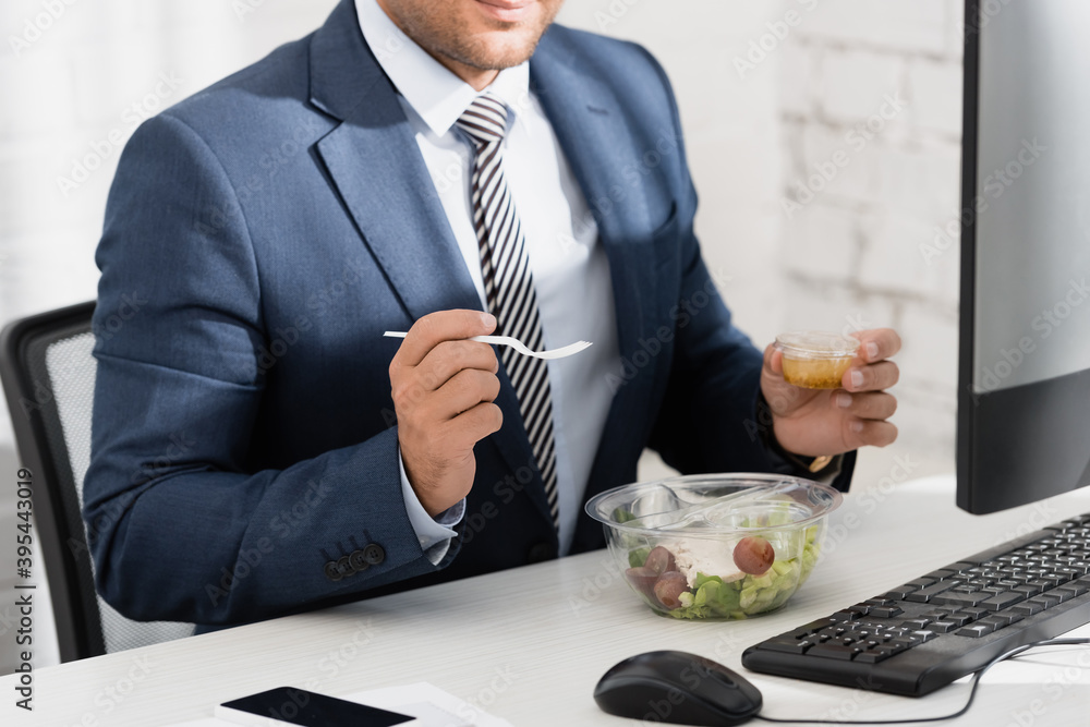 Cropped view of businessman holding plastic fork and container with sauce, while sitting at table with meal in bowl, stock image Cropped view of businessman holding plastic fork and container with sauce, while sitting at table with meal in bowl, stock image