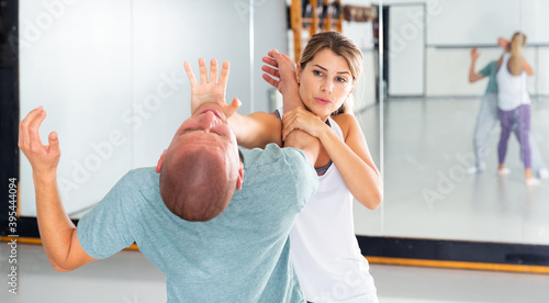 Concentrated girl practicing effective self defence techniques with coach in training room, using palm to launch blow in chin..