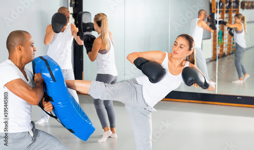 Sporty Diligent serious woman in boxing gloves training with trainer in gym