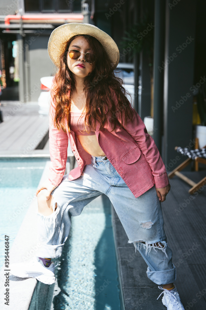 Fashion portrait of asian woman wearing sunglasses, pink jacket, and hat on street.