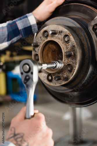 cropped view of mechanic fixing wheel hub with wrench on blurred 