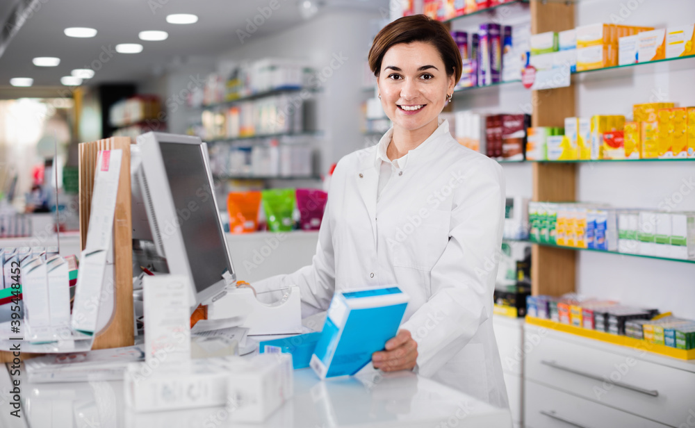 Cheerful female pharmacist offering help in choosing at counter in pharmacy