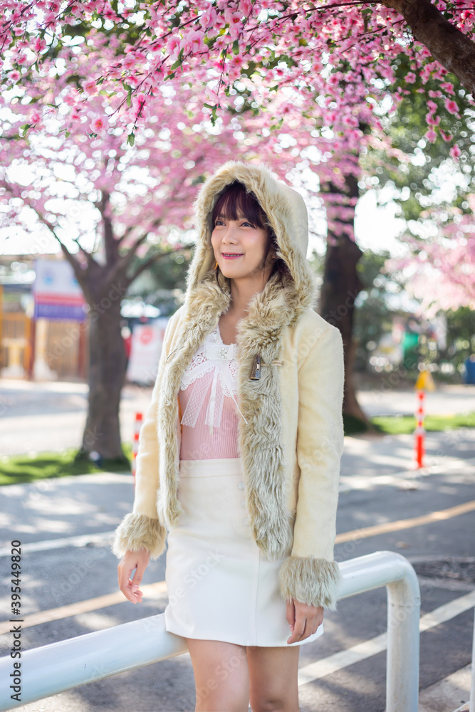Happy young girl in a wool sweateron is enjoy and relax on a background with sakura cherry blossoms tree on vacation while spring in asian. Travel concept
