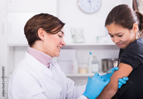 urse in medical gown and gloves vaccinates teenage girl in treatment room