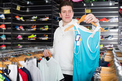 Fotografija Adult man is choosing tennis T-shirt in the sportive store