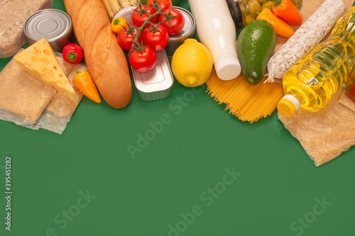 Different groceries or food donations on green background with copyspace - pasta, fresh vegatables, canned food, baguette, cooking oil, tomatoes, cheese. Food bank or food delivery concept