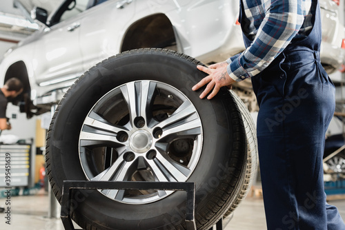 cropped view of man taking wheel near auto raised on car lift on blurred 