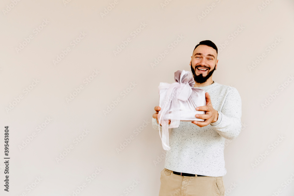 Portrait of a dark-haired European man with a gift in his hands. Happy young man with a beard on a beige background. Holiday concept. Portrait of a dark-haired European man with a gift in his hands. Happy young man with a beard on a beige background. Holiday concept.